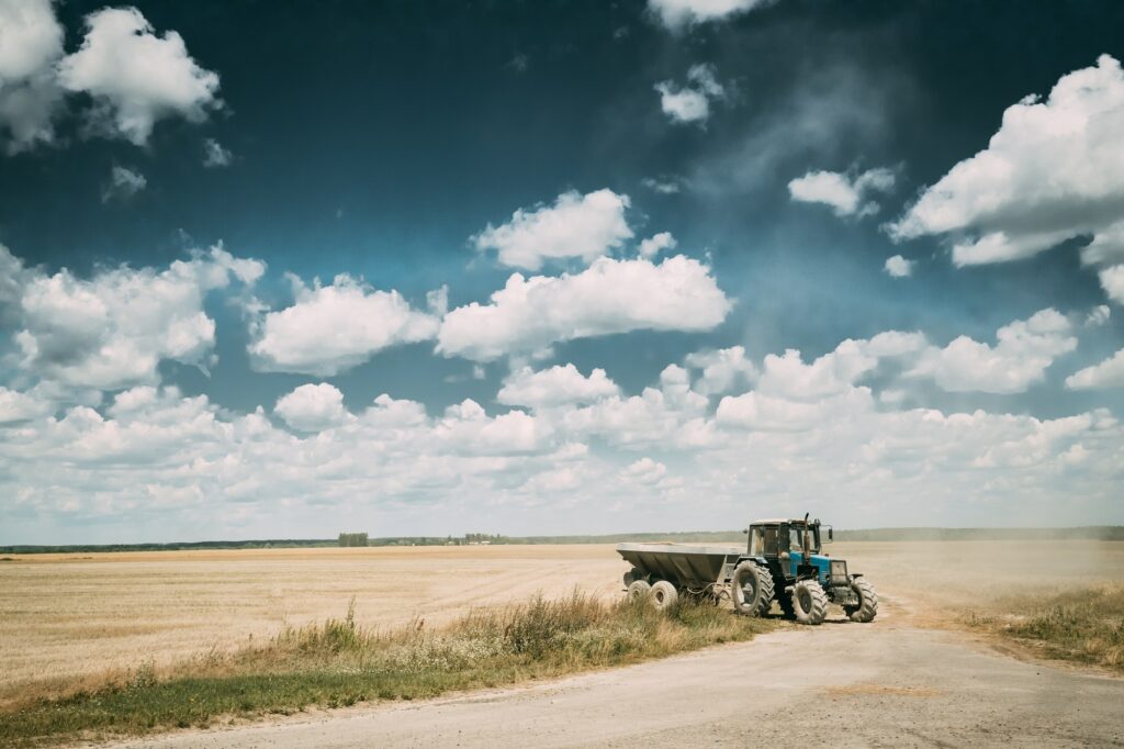 Tractor With Cart In Motion On Country Road In Summer Season. Ag